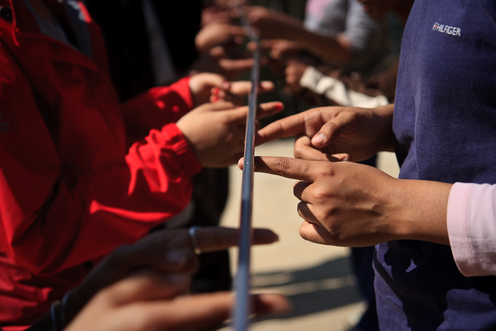 Ensuring that everyone’s index fingers are always in contact with the ‘Magic Stick’, the group has to lower it to the ground. Add more to the group and the task gets exponentially harder. 